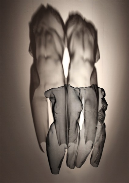 Torso sculptures are suspended with large shadow reflections on the back wall