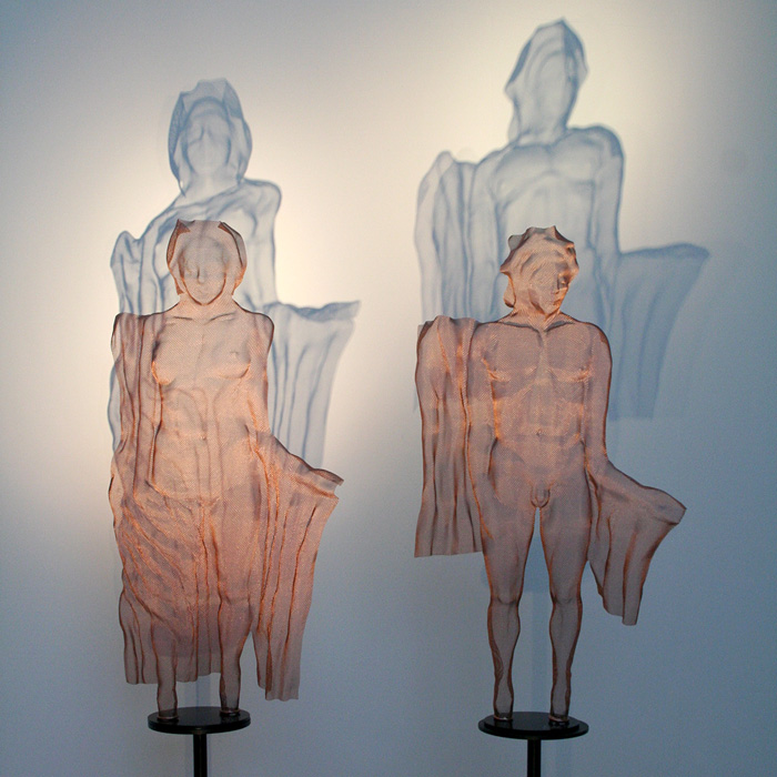 Two bronze-coloured mesh-sculptures with drapery and their shadow reflections
