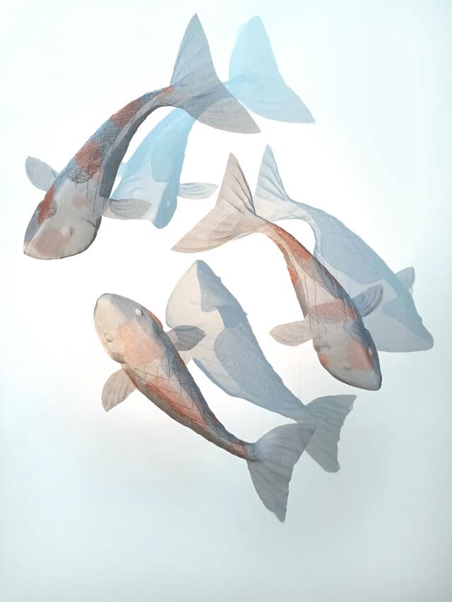 Three fish sculptures made from stainless steel mesh floating in front of a wall