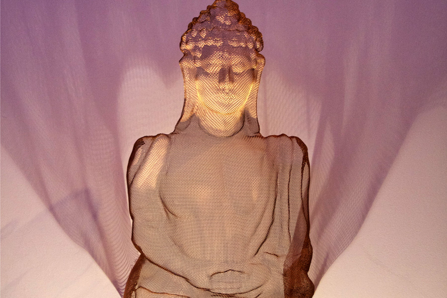 Detail of a meditating Buddha figure in bronze-mesh surrounded by its spotlight shadows