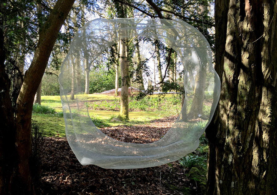 Abstract white wire-mesh sculpture with figurative elements between-trees at the Hannah Peschar Sculpture Garden, Surrey, UK