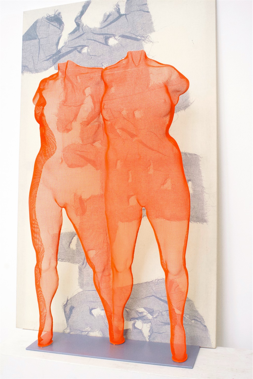 A red wire-figure depicting two female figures in front of an abstract painting