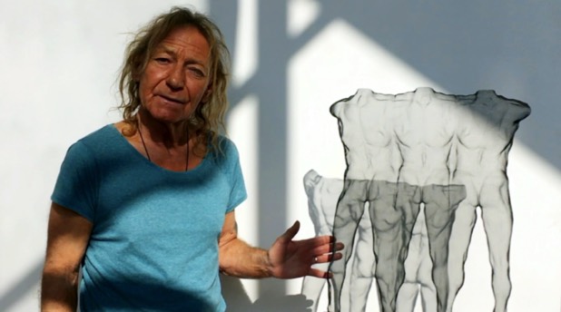 A sculptor explains his multiple wire-mesh figures which is seen in a sunny studio. The black sculpture made from steel is semi-transparent and produces shadows on the white background